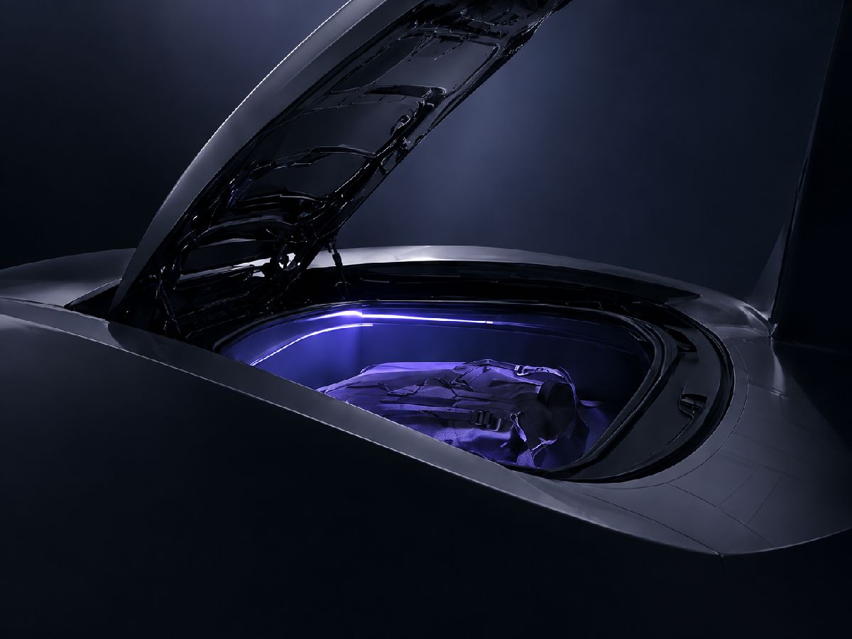 A close-up of the open front trunk at night, a backpack inside, lit in violet